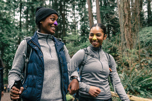 Two young African American women hiking in the woods wearing different shades of Noz reef safe and cruelty-free sunscreen.